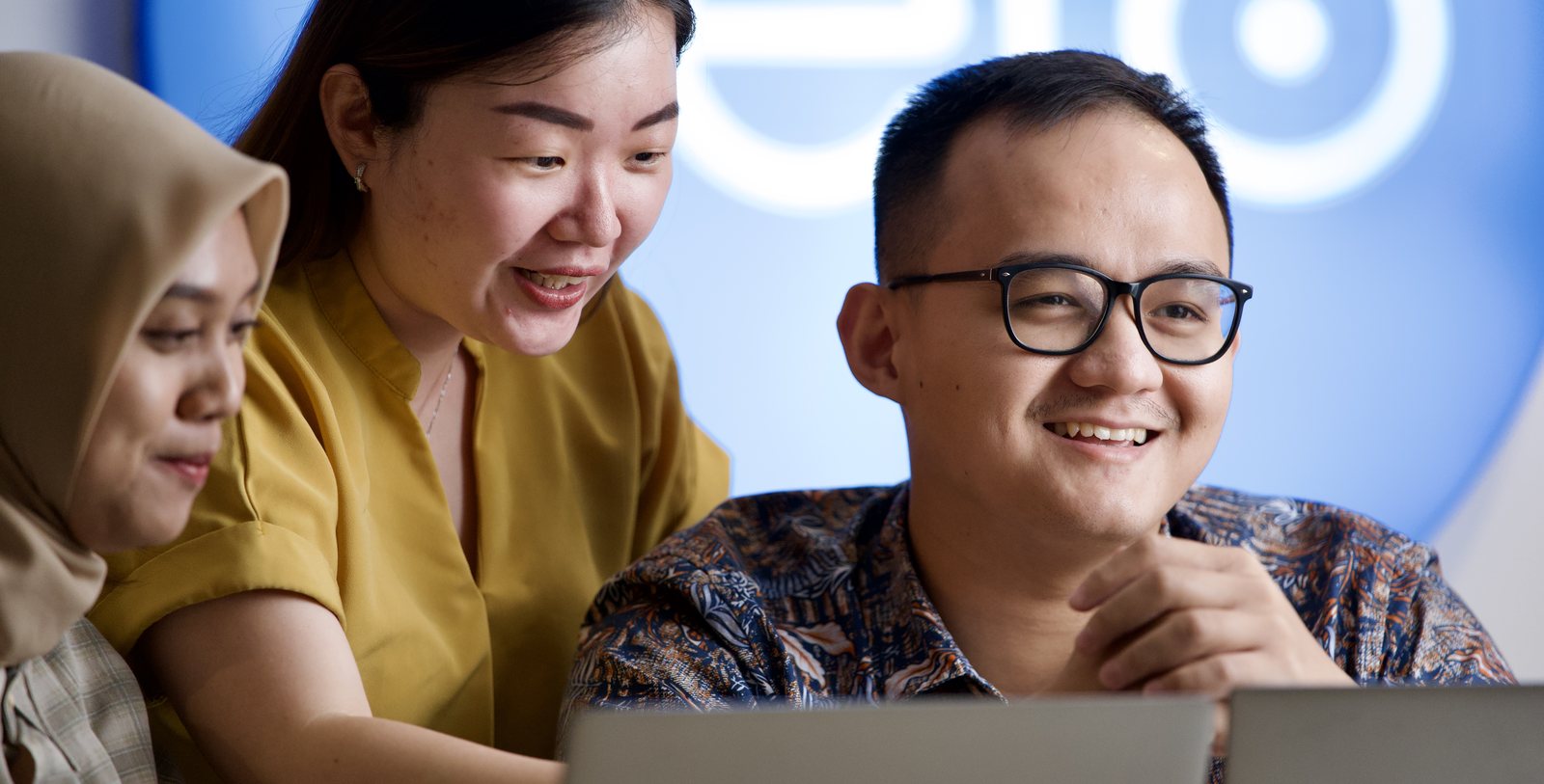 Three Logiframe colleagues looking at a laptop together in the Indonesia office, in front of a Xero-branded wall.