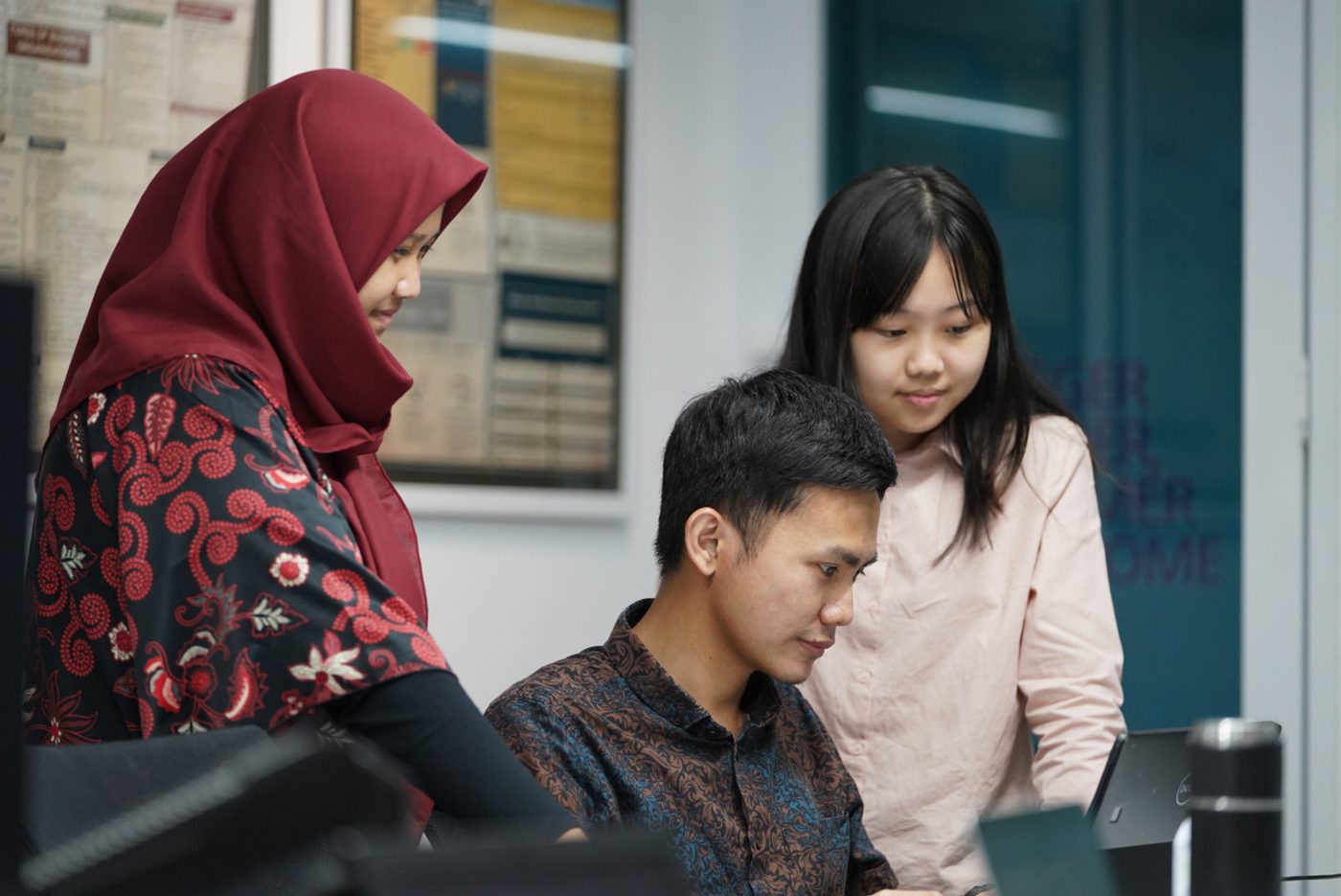 Three colleagues gathered at a desk, working through something together on screen.