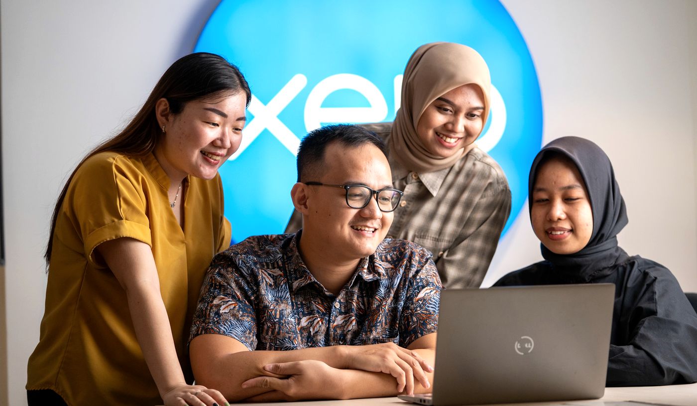 Four Logiframe team members smiling around a laptop in front of the Xero sign.